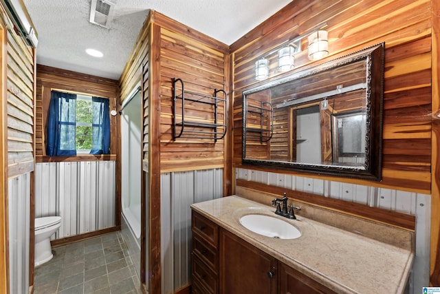 bathroom with toilet, vanity, wooden walls, and a textured ceiling