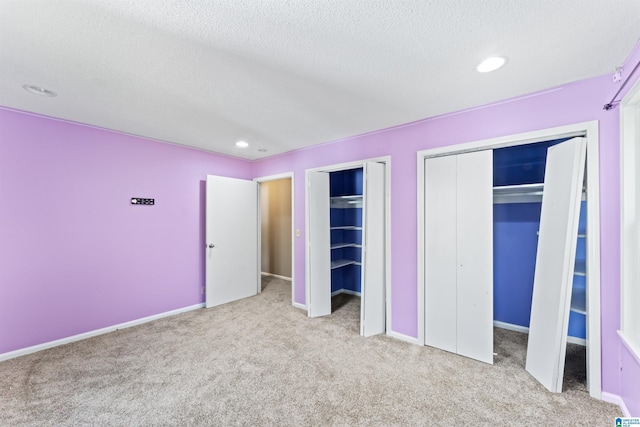 unfurnished bedroom featuring light colored carpet, a textured ceiling, and two closets