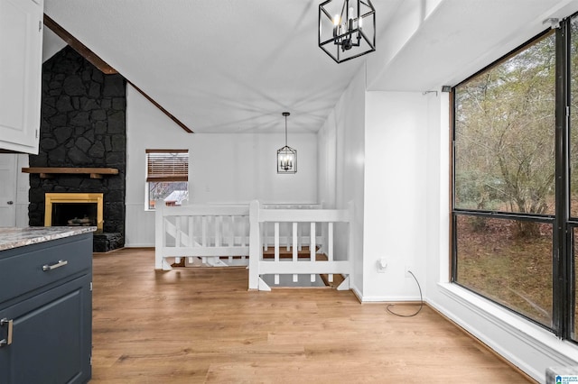 interior space with an inviting chandelier, a stone fireplace, plenty of natural light, and light hardwood / wood-style flooring