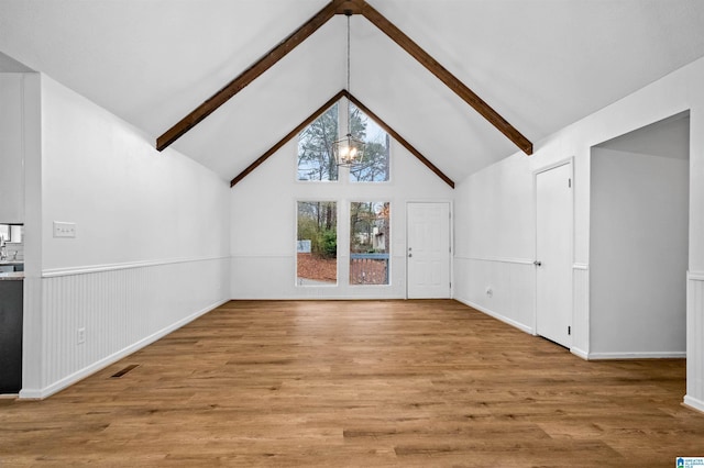 unfurnished living room featuring vaulted ceiling with beams, light hardwood / wood-style floors, and a chandelier