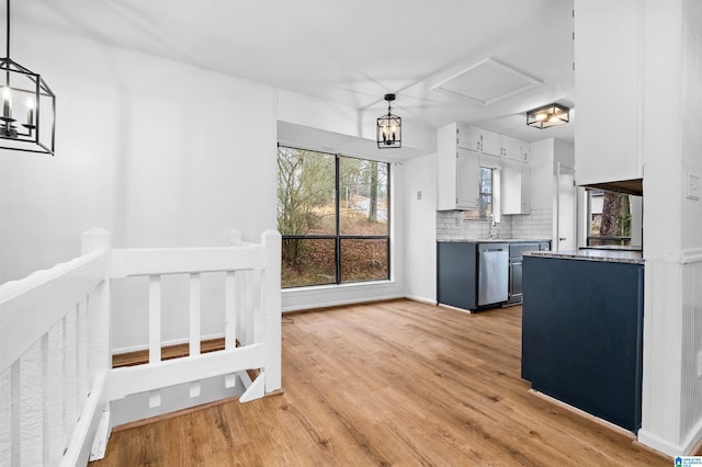 kitchen with pendant lighting, tasteful backsplash, white cabinets, stainless steel dishwasher, and light wood-type flooring