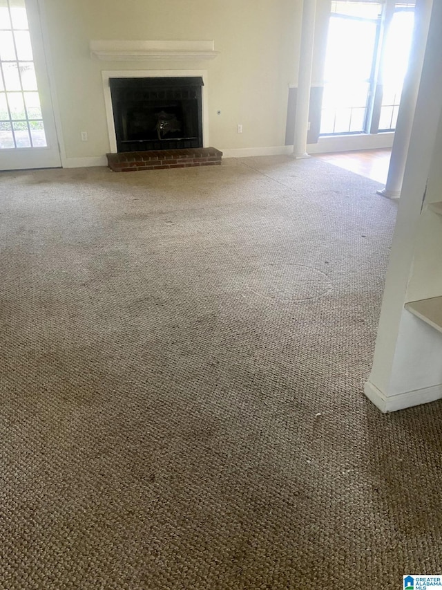 unfurnished living room with a brick fireplace, a healthy amount of sunlight, and carpet flooring