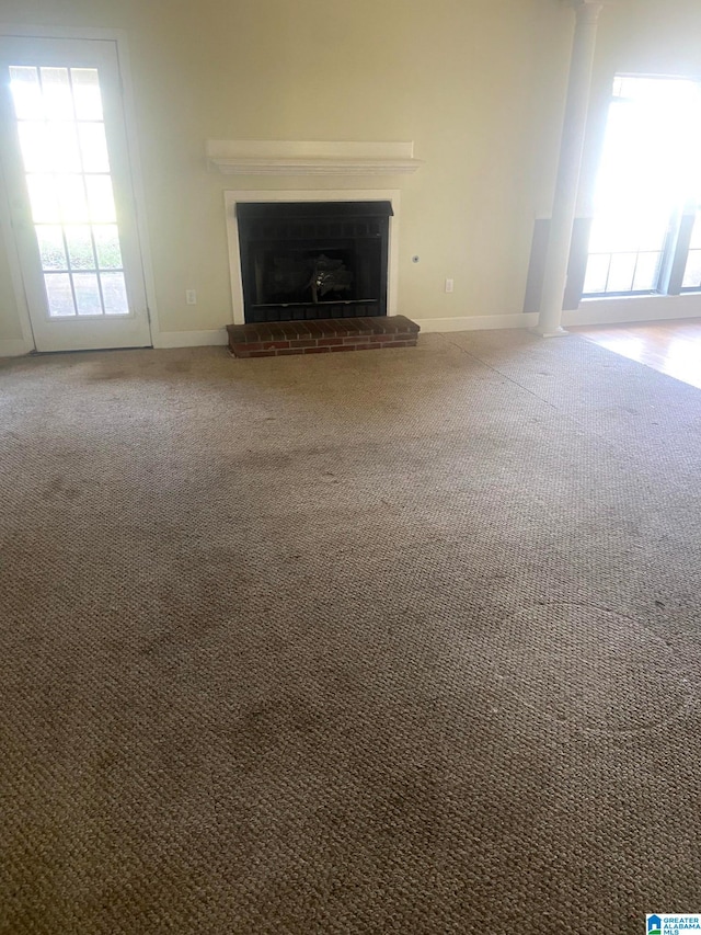 unfurnished living room with a brick fireplace, a wealth of natural light, and carpet flooring