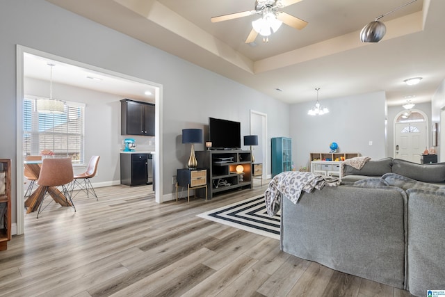 living room featuring a raised ceiling, ceiling fan with notable chandelier, and light hardwood / wood-style flooring