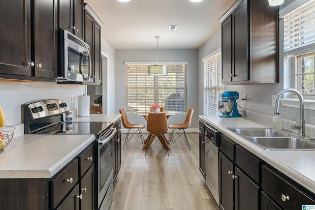 kitchen with sink, light hardwood / wood-style flooring, appliances with stainless steel finishes, dark brown cabinetry, and decorative light fixtures