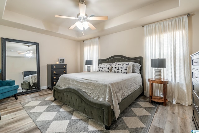 bedroom with light hardwood / wood-style flooring, a raised ceiling, and ceiling fan