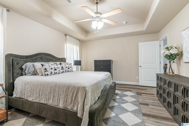 bedroom with wood-type flooring, ceiling fan, and a tray ceiling