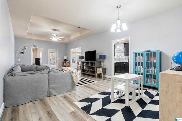 living room featuring hardwood / wood-style flooring, ceiling fan with notable chandelier, and a raised ceiling