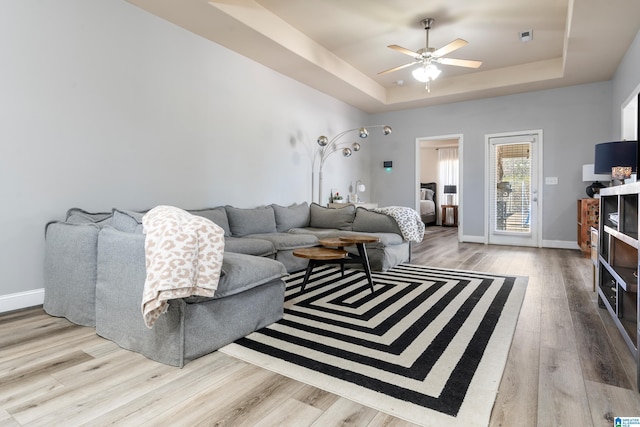 living room featuring light hardwood / wood-style floors, a raised ceiling, and ceiling fan