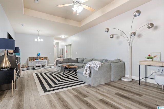 living room with a raised ceiling, wood-type flooring, and ceiling fan with notable chandelier