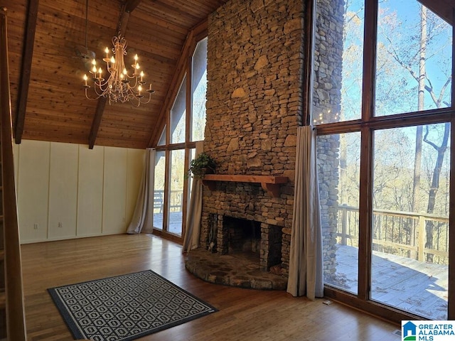 unfurnished living room with a stone fireplace, high vaulted ceiling, hardwood / wood-style flooring, a notable chandelier, and wood ceiling