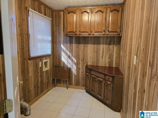 interior space featuring hookup for a washing machine, light tile patterned flooring, cabinets, and wood walls