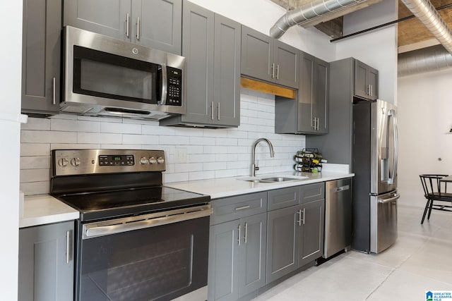 kitchen with tasteful backsplash, stainless steel appliances, gray cabinets, and sink