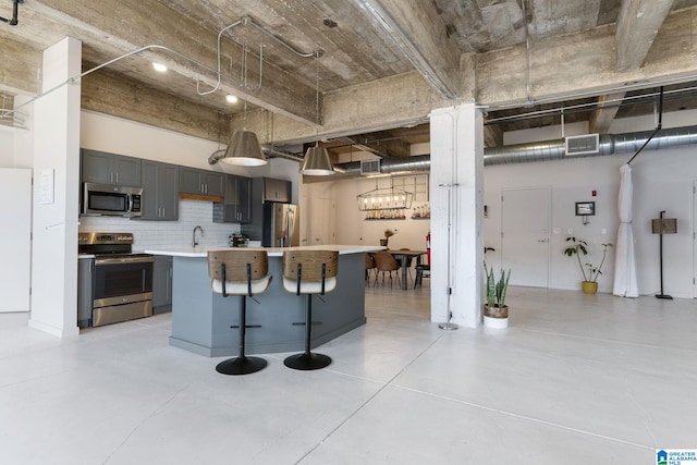 kitchen with a kitchen island, appliances with stainless steel finishes, gray cabinetry, backsplash, and a kitchen bar