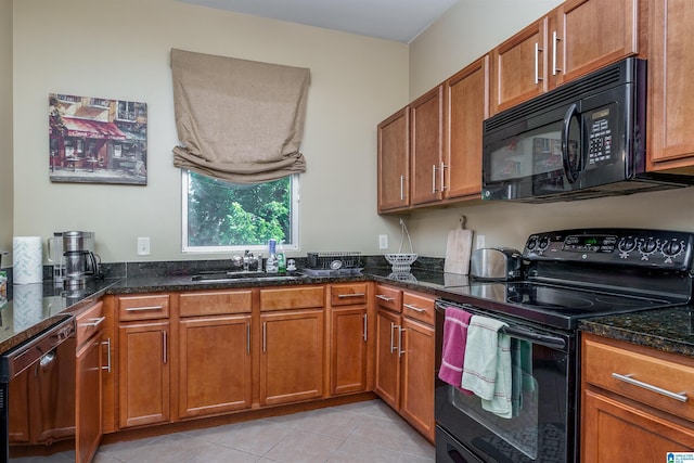 kitchen featuring a sink, dark stone counters, black appliances, and brown cabinetry