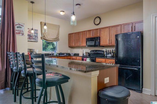 kitchen with decorative light fixtures, a breakfast bar, light tile patterned floors, brown cabinets, and black appliances