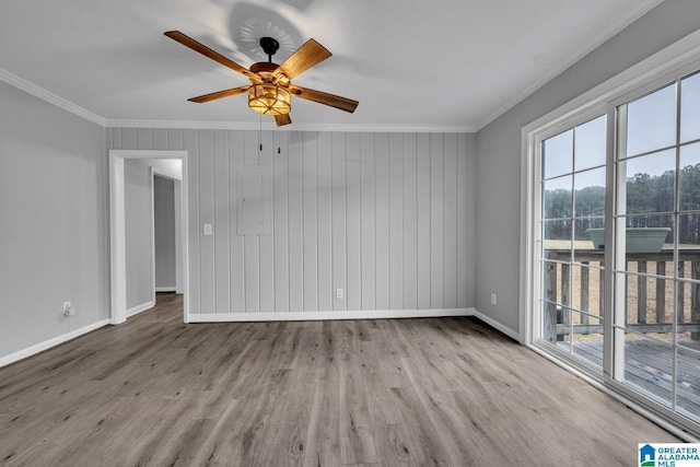 spare room featuring ornamental molding, wooden walls, light hardwood / wood-style flooring, and a wealth of natural light