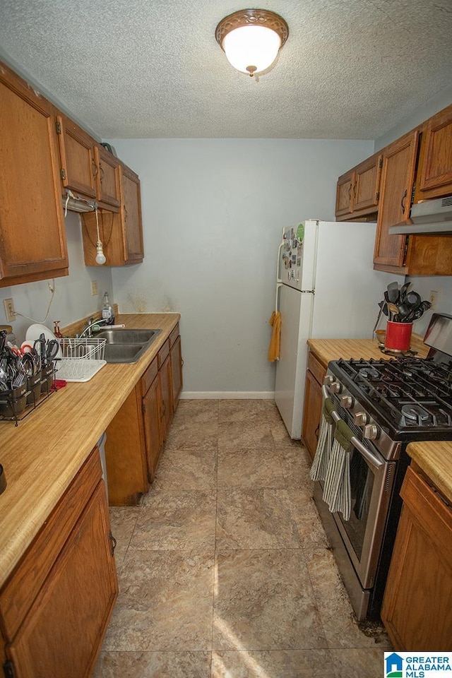 kitchen featuring white fridge, stainless steel gas range, sink, and a textured ceiling