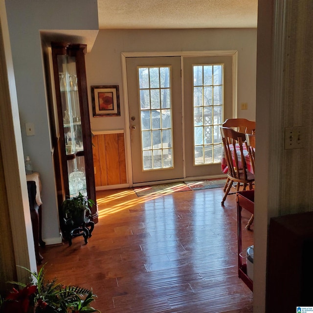 doorway to outside featuring a textured ceiling, wooden walls, and wood-type flooring