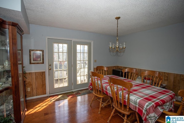 dining area featuring hardwood / wood-style flooring, an inviting chandelier, a textured ceiling, and wooden walls