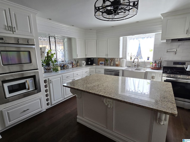 kitchen featuring sink, stainless steel appliances, light stone counters, white cabinets, and a kitchen island