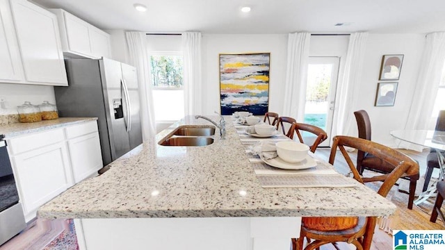 kitchen featuring stainless steel refrigerator with ice dispenser, white cabinetry, an island with sink, and sink