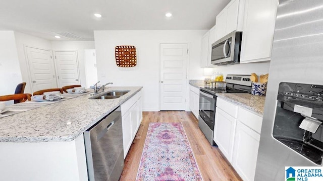 kitchen with stainless steel appliances, a kitchen island with sink, sink, and white cabinets