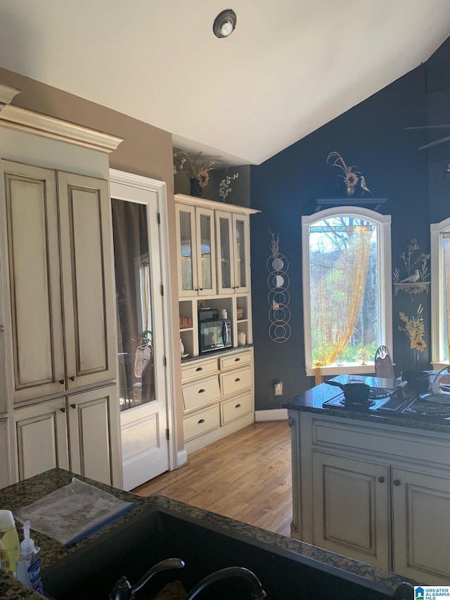 kitchen featuring vaulted ceiling, cream cabinets, dark stone counters, and light hardwood / wood-style flooring