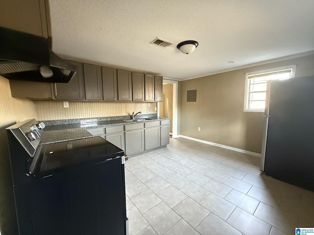 kitchen with a textured ceiling, stainless steel refrigerator, light tile patterned floors, sink, and electric range oven