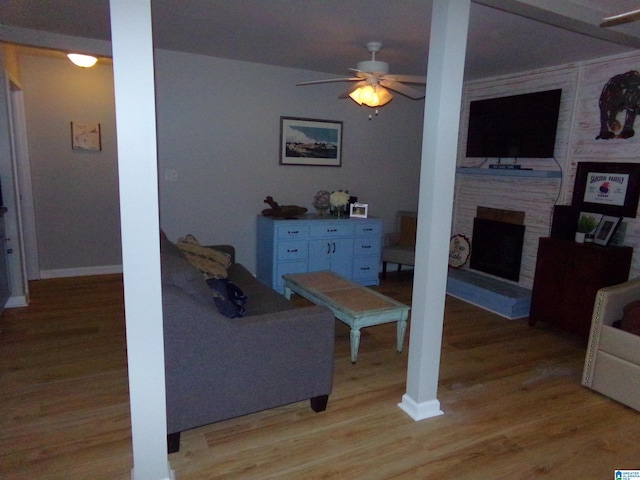 living room with light wood-type flooring, a fireplace, a ceiling fan, and baseboards