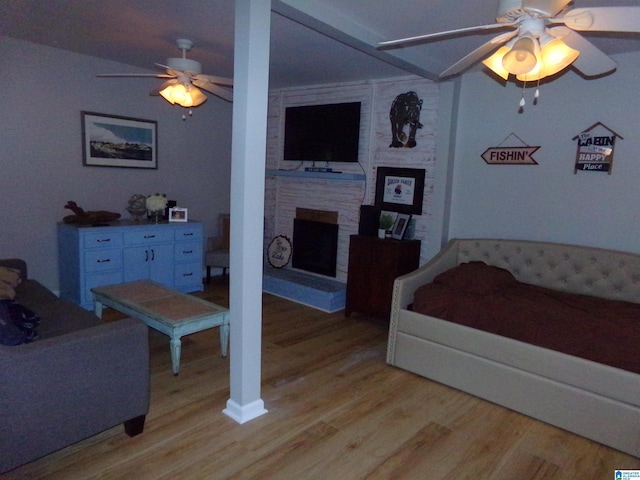 bedroom featuring light wood finished floors, a brick fireplace, and a ceiling fan