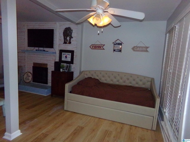 bedroom featuring a ceiling fan, a large fireplace, and wood finished floors