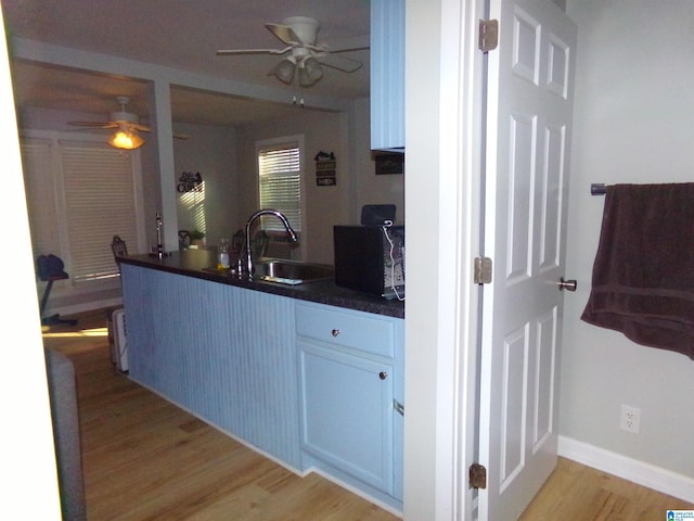 kitchen with ceiling fan, light wood-style flooring, a peninsula, a sink, and dark countertops