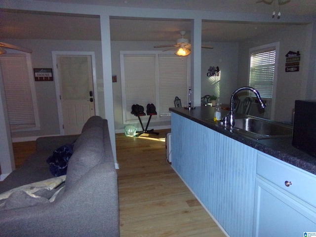 kitchen featuring dark countertops, white cabinets, a sink, and light wood-style flooring