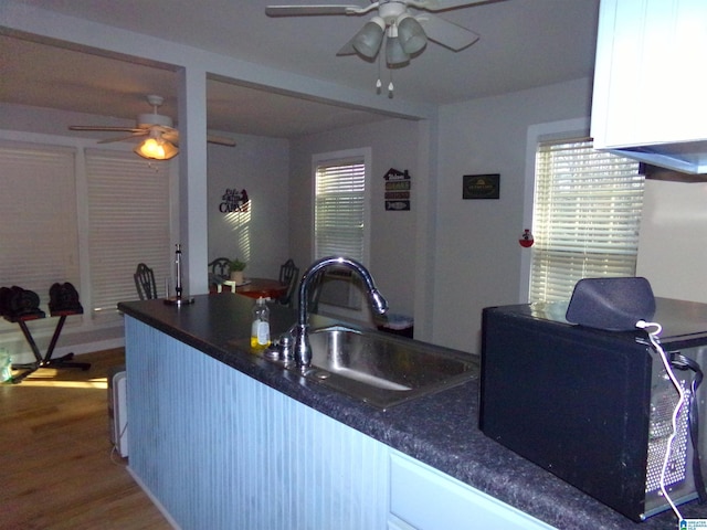 kitchen with dark countertops, black microwave, a sink, and wood finished floors