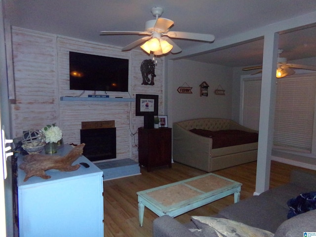 living room with ceiling fan, a fireplace with raised hearth, and wood finished floors