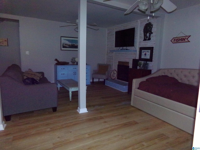 bedroom featuring a brick fireplace, ceiling fan, and wood finished floors