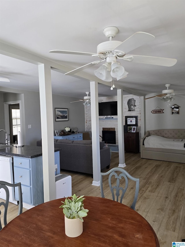 dining area featuring a fireplace, light wood-style flooring, and a ceiling fan