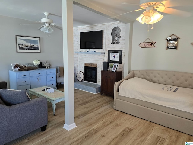 bedroom with light wood-style floors, a large fireplace, and a ceiling fan