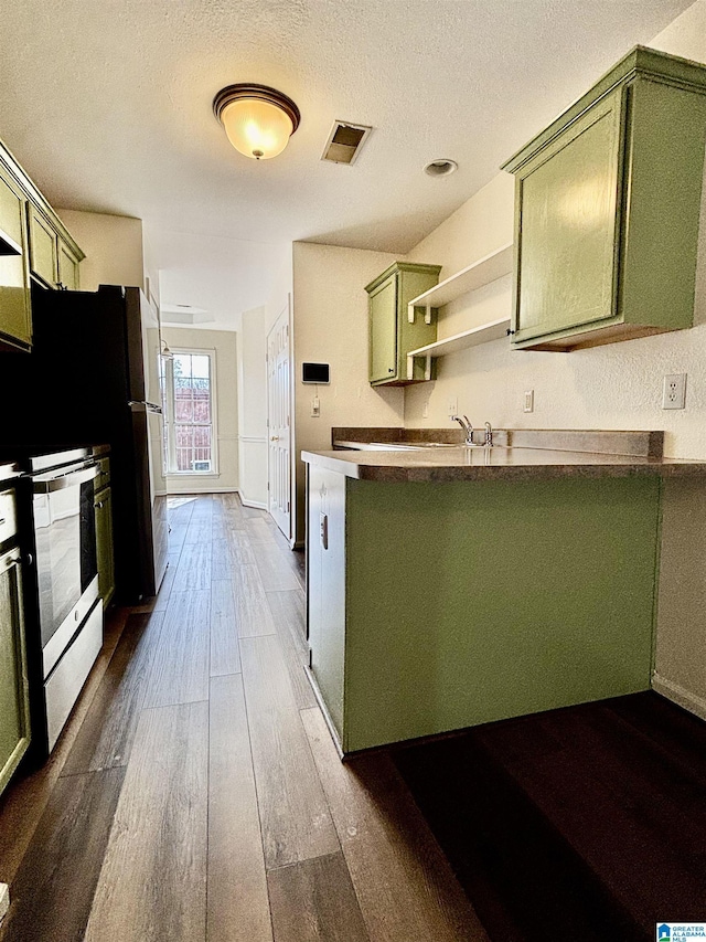 kitchen featuring dark wood-type flooring, green cabinets, a textured ceiling, stainless steel electric range oven, and kitchen peninsula