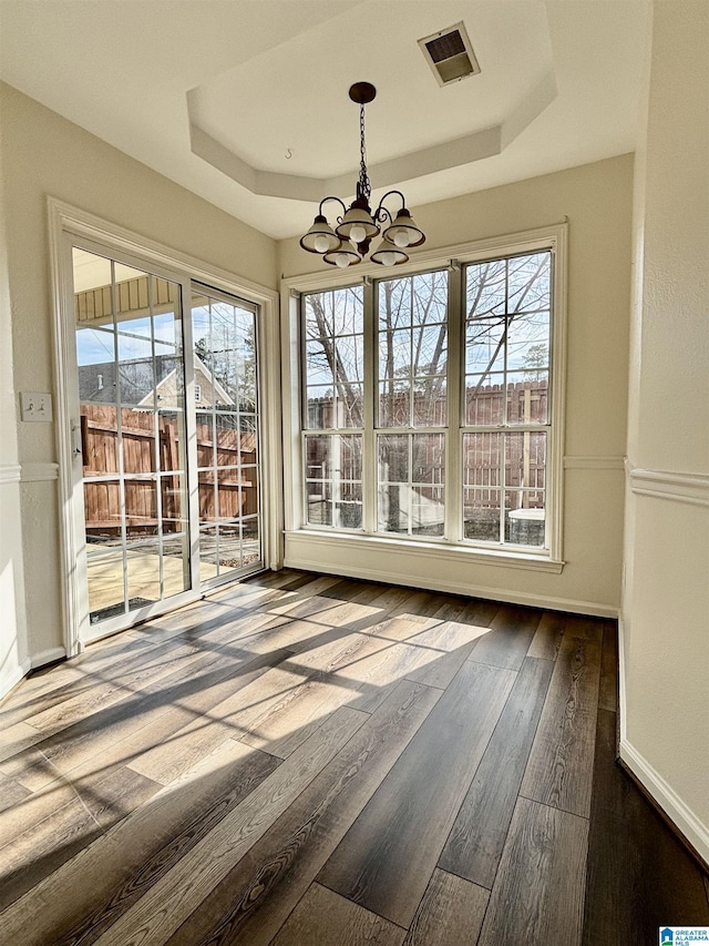 unfurnished dining area featuring dark wood-type flooring, a raised ceiling, and a chandelier