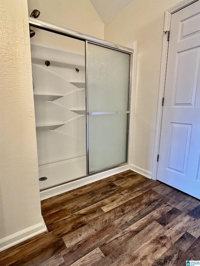 bathroom with wood-type flooring, vaulted ceiling, and walk in shower