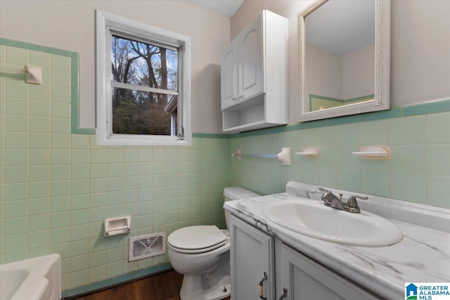 bathroom with tile walls, vanity, toilet, and a tub to relax in