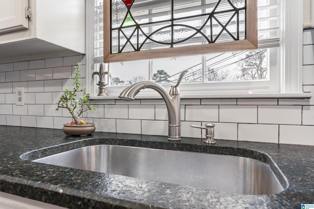 interior details with tasteful backsplash, white cabinetry, sink, and dark stone countertops