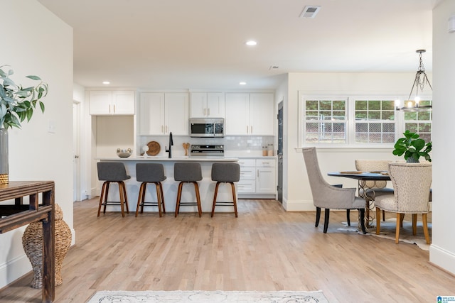 kitchen with appliances with stainless steel finishes, pendant lighting, tasteful backsplash, white cabinetry, and light hardwood / wood-style floors