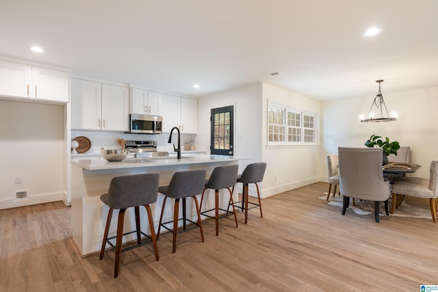 kitchen with decorative light fixtures, white cabinetry, sink, a kitchen island with sink, and stainless steel appliances