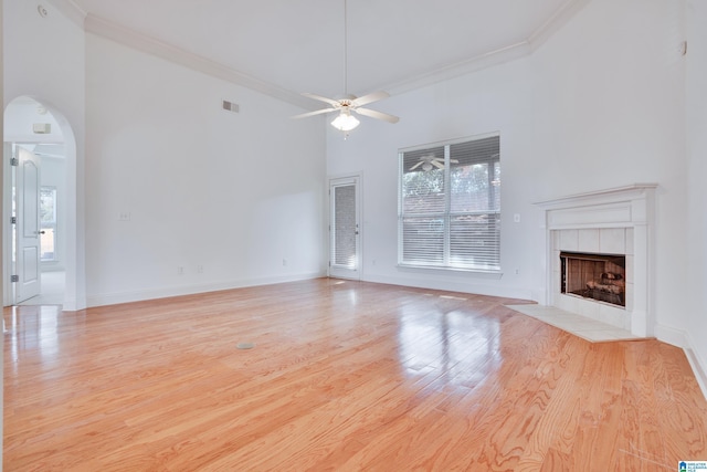 unfurnished living room with crown molding, light hardwood / wood-style flooring, ceiling fan, a tiled fireplace, and a high ceiling