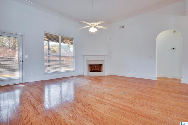 unfurnished living room with crown molding, ceiling fan, a high ceiling, a fireplace, and light hardwood / wood-style floors