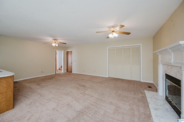 unfurnished living room featuring ceiling fan, a fireplace, light carpet, and a textured ceiling