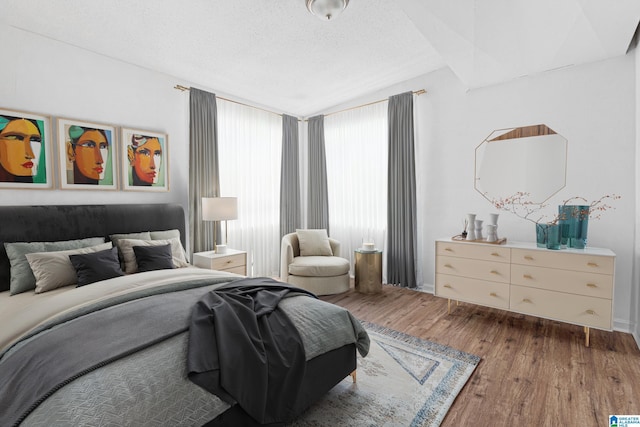 bedroom featuring wood-type flooring, lofted ceiling, and a textured ceiling